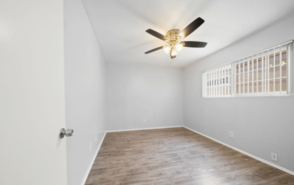 A room with a ceiling fan and a window with bars.